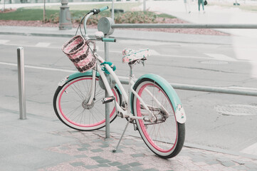 Women's bicycle parked on the street with a lock. Vintage bicycle in mint and pink colors with a basket stay on the pavement in Moscow city