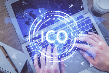 Double exposure of man's hands typing over computer keyboard and crypto currency theme hologram...