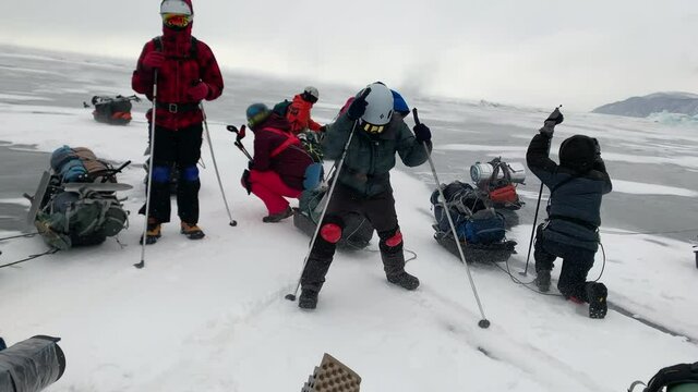 A group of tourists stands and tries to resist the strong wind that blows them away during a winter hike with sleds and backpacks on the frozen Lake Baikal.
