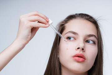 Beautiful young girl cleanses the skin getting rid of acne while holding a dropper with serum in...