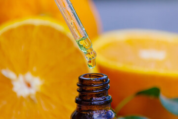 Essential orange oil in a bottle, fresh fruit pieces on the background. Natural flavors.