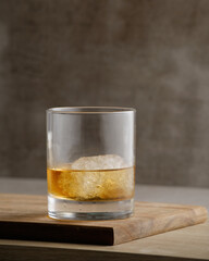 A glass of whiskey with ice on wooden plank and gray background.