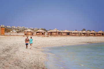 mixed couple walking along the coast along the straw bungalows of a hippie Bedouin camps on the coast of the Sinai Peninsula of Egypt