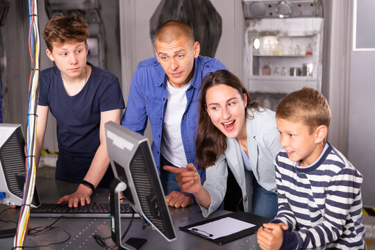 Happy Interested Family With Teen Sons Trying To Get Out Of Closed Space Of Escape Room Stylized As Abandoned Bunker, Using Computer