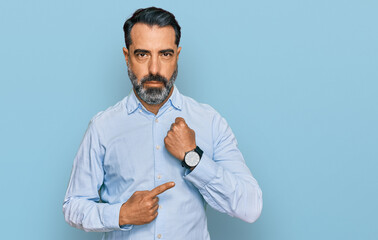 Middle aged man with beard wearing business shirt in hurry pointing to watch time, impatience,...