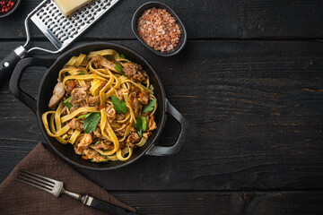Tagliatelle with chanterelles and stewed rabbit, in frying cast iron pan or pot, on black wooden table , top view flat lay, with copy space for text