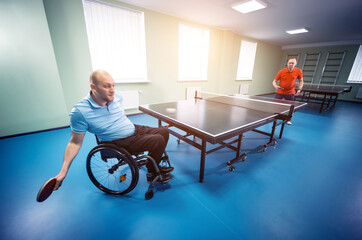 Adult disabled man in a wheelchair play at table tennis with his coach