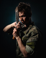 Portrait of a soldier in scars and combat coloring, holding a machete on a black background