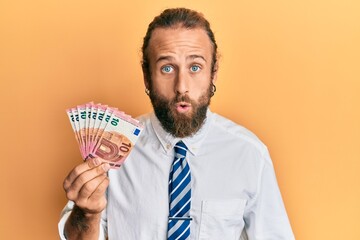Handsome business man with beard and long hair holding bunch of 10 euro banknotes scared and amazed...