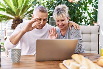 Senior caucasian couple having breakfast and video call using laptop at the terrace.