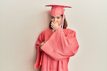 Young caucasian woman wearing graduation cap and ceremony robe smelling something stinky and disgusting, intolerable smell, holding breath with fingers on nose. bad smell - obrazy, fototapety, plakaty