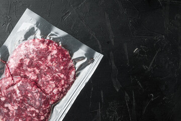 Vacuum beef cutlet sealed airtight pack, on black stone background, top view flat lay, with copy space for text