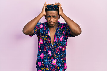 Young black man wearing hawaiian shirt and sunglasses suffering from headache desperate and stressed because pain and migraine. hands on head.