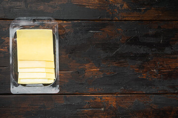 Yellow cheese slices of cheddar, in plastic pack, on old dark  wooden table background, top view...