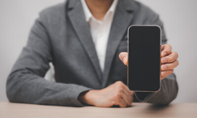 Businessman hand holding mobile white blank screen, Mock up cell mobile smart phone  in suit holds mobile phone with blank white screen on dark blue background,online business concept