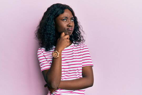 Beautiful african young woman wearing casual striped t shirt thinking concentrated about doubt with finger on chin and looking up wondering