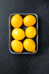 Ripe lemons, in plastic tray, on black background