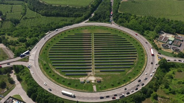 Car traffic on the motorway top view. Large roundabout in the forest aerial view. Solar panels in the center of a circular automobile ring. Italy roads aerial view. Solar panels by the road.