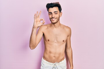 Fototapeta premium Young hispanic man wearing swimwear shirtless smiling positive doing ok sign with hand and fingers. successful expression.