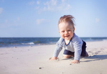 happy, smiling boy on the beach. 8 month old blond boy crawling on the beach