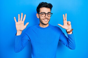 Naklejka premium Young hispanic man wearing casual clothes and glasses showing and pointing up with fingers number eight while smiling confident and happy.