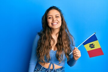 Young hispanic girl holding moldova flag looking positive and happy standing and smiling with a confident smile showing teeth