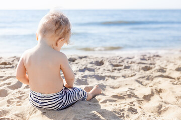 10 month old blond boy playing with sand on the beach. back view
