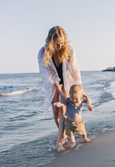 young mother teaches baby to walk on the beach