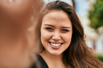 Naklejka premium Young hispanic woman smiling happy making selfie by the camera at the city.