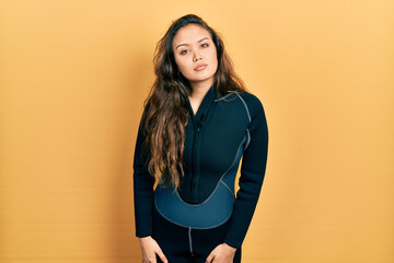 Young hispanic girl wearing diver neoprene uniform relaxed with serious expression on face. simple...