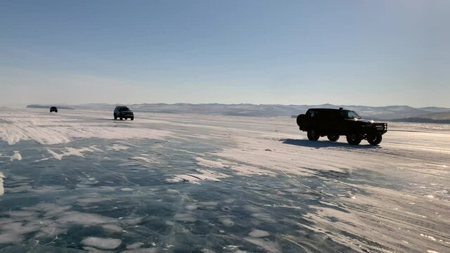 A convoy of off-road vehicles rides on the ice of frozen Lake Baikal. SUVs are driving on a road made of ice. Traveling by car in winter