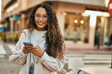 Young latin woman smiling happy using smartphone at the city.