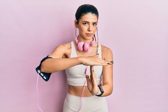 Young Hispanic Woman Wearing Gym Clothes And Using Headphones Doing Time Out Gesture With Hands, Frustrated And Serious Face