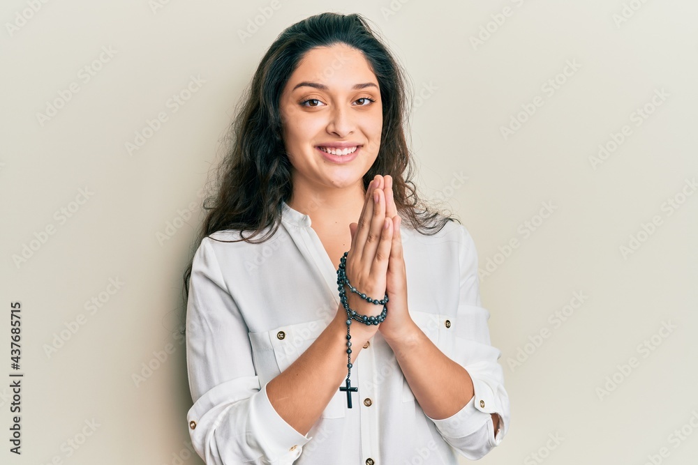 Wall mural beautiful hispanic woman playing with catholic rosary smiling with a happy and cool smile on face. s