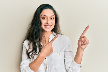 Beautiful middle eastern woman wearing casual clothes smiling and looking at the camera pointing with two hands and fingers to the side.