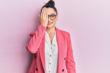 Beautiful middle eastern woman wearing business jacket and glasses covering one eye with hand, confident smile on face and surprise emotion.