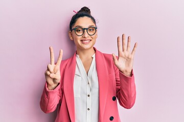 Beautiful middle eastern woman wearing business jacket and glasses showing and pointing up with fingers number seven while smiling confident and happy.