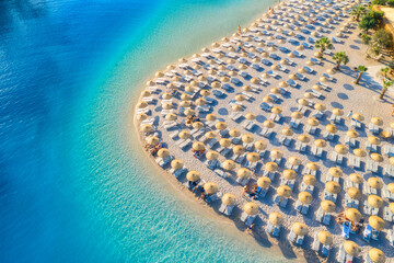 Aerial view of sea, empty sandy beach with sun beds and umbrellas at sunset in summer. Blue lagoon in Oludeniz, Turkey. Tropical landscape with clear turquoise water, deck chair. Travel and leisure