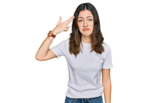 Young beautiful woman wearing casual white t shirt shooting and killing oneself pointing hand and fingers to head like gun, suicide gesture.
