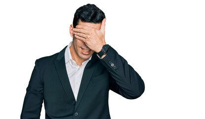 Handsome hispanic man wearing business clothes smiling and laughing with hand on face covering eyes for surprise. blind concept.
