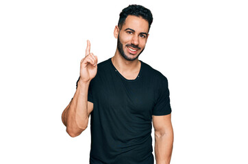 Hispanic man with beard wearing casual black t shirt showing and pointing up with finger number one while smiling confident and happy.