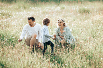Happy young family spending time together outside in green meadow with flower outdoors. The concept of family holiday.