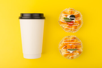 Creative flat lay with White cardboard coffee cup and two mini cakes with pieces of fruits and...