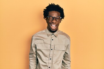 Young african american man wearing casual clothes and glasses winking looking at the camera with sexy expression, cheerful and happy face.