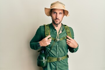 Fototapeta premium Handsome man with beard wearing explorer hat and backpack relaxed with serious expression on face. simple and natural looking at the camera.