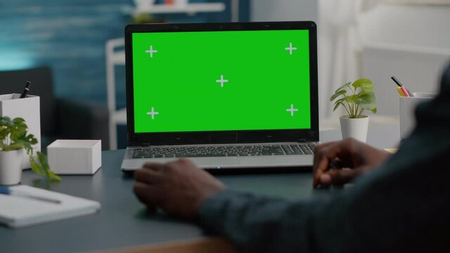 Close up of african american man using green screen laptop in bright living room. Computer usir with isolated chroma key mockup mock up display