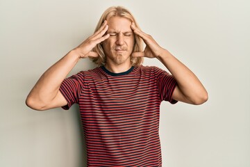 Caucasian young man with long hair wearing casual striped t shirt with hand on head, headache because stress. suffering migraine.