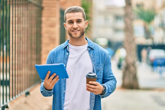 Young caucasian man smiling happy using touchpad and drinking coffee at the city.