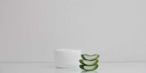 White jar with cosmetic cream and aloe vera leaves on a white background. Spa concept.