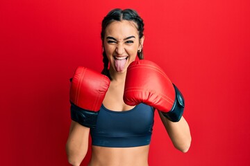 Young brunette girl using boxing gloves sticking tongue out happy with funny expression.